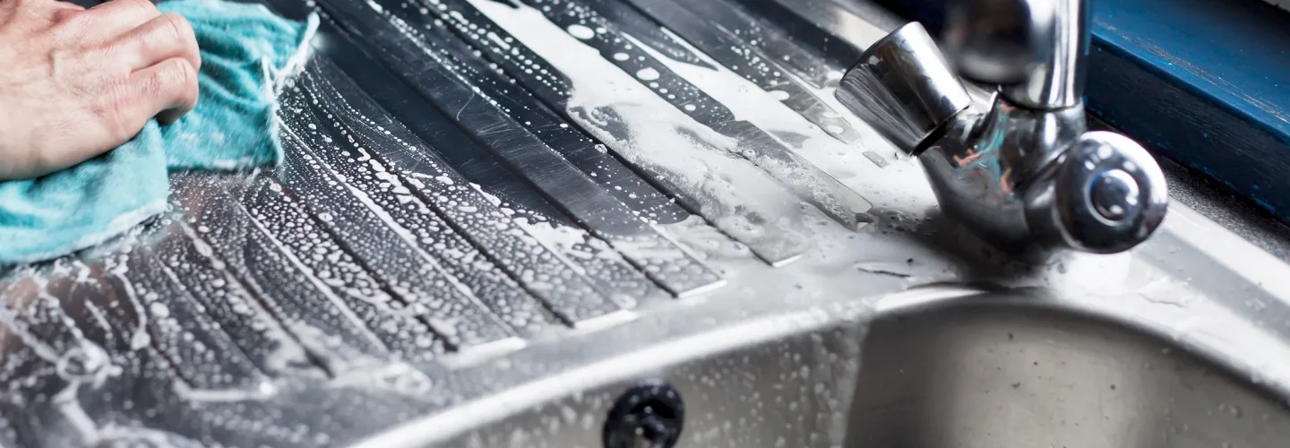 Person scrubbing a steel sink with soap